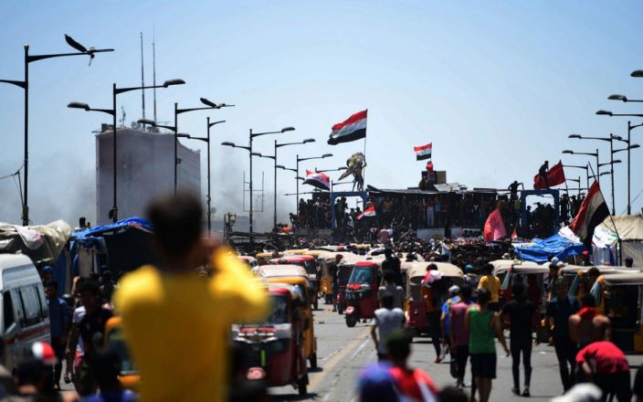 متظاهرون يحملون العلم الوطني العراقي وهم يتجمعون على جسر الجمهورية ، مما يؤدي إلى مقر الحكومة العراقية داخل المنطقة الخضراء المشددة - شاترستوك