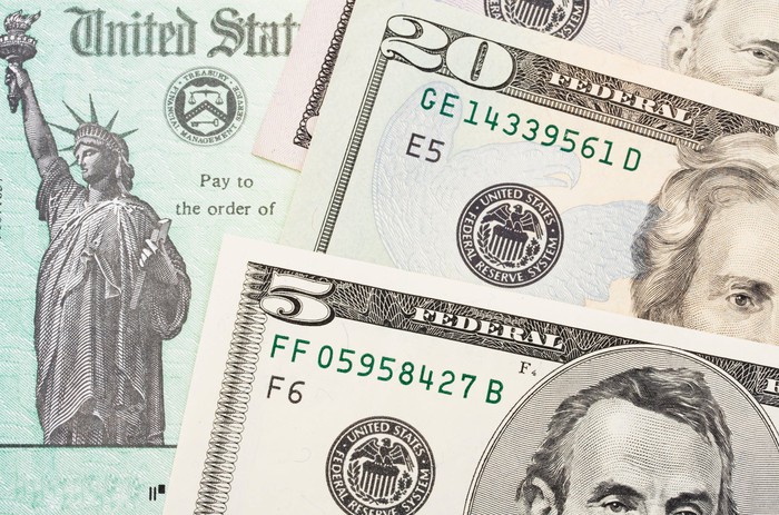 كومة منتشرة من الفواتير النقدية تغطي جزئياً شيك الخزانة الأمريكية.