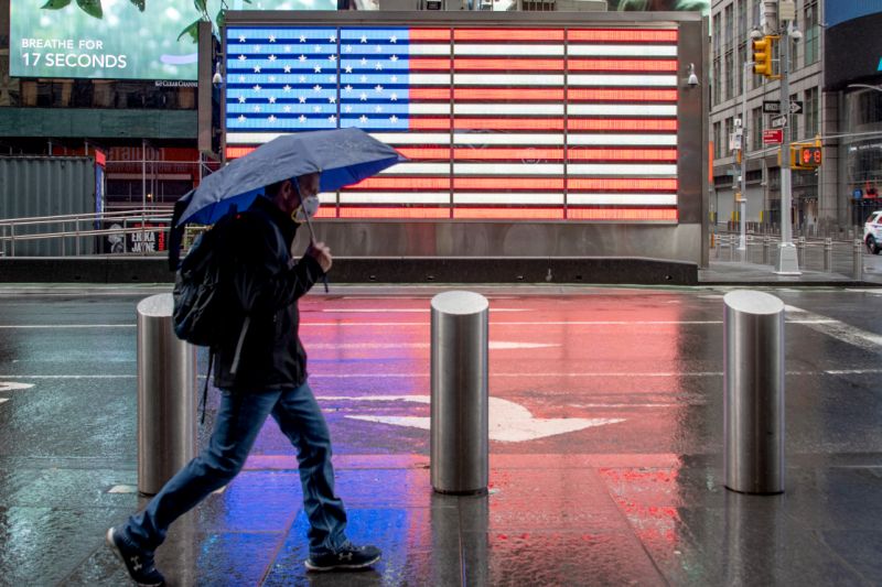 نيويورك ، نيويورك - 06 أيار / مايو: رجل يرتدي قناعاً يمشي مع مظلة في ميدان التايمز بالقرب من العلم الأمريكي وسط جائحة فيروس كورونا في 6 مايو 2020 في مدينة نيويورك. انتشرت COVID-19 في معظم البلدان في جميع أنحاء العالم ، مما أودى بحياة أكثر من 263،000 مع أكثر من 3.8 مليون حالة. (تصوير أليكسي روزنفيلد / غيتي إيماجز)