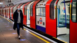 امرأة ترتدي معدات الوقاية الشخصية (PPE) ، بما في ذلك قناع الوجه كإجراء وقائي ضد COVID-19 ، تمشي على طول المنصة إلى جانب قطار مترو أنفاق لندن في ساعة الذروة الصباحية ، في 11 مايو 2020